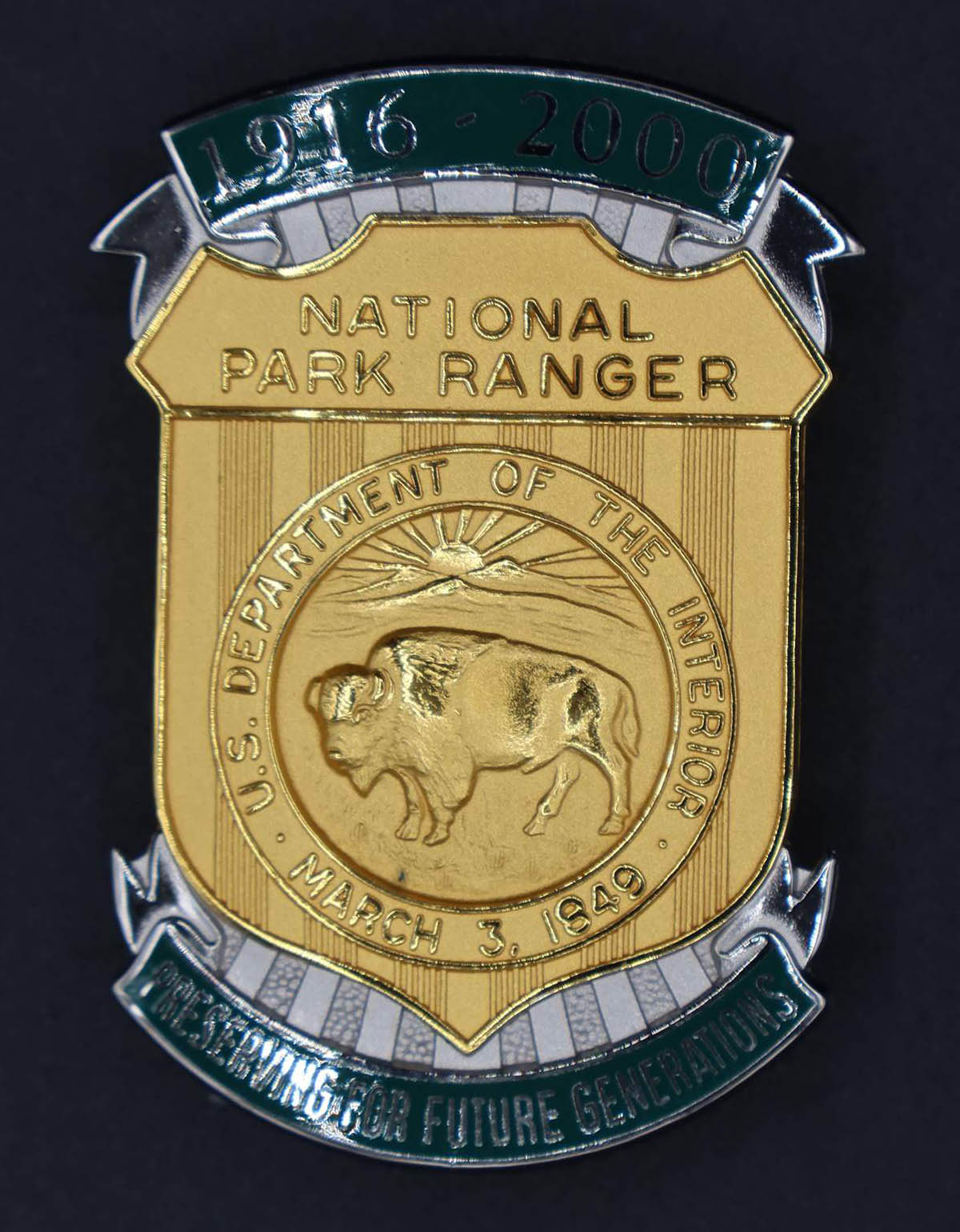 Gold shield-shaped bison badge marked National Park Ranger. Green banners at top and bottom read 1916-2000 and Preserving for Future Generations. 