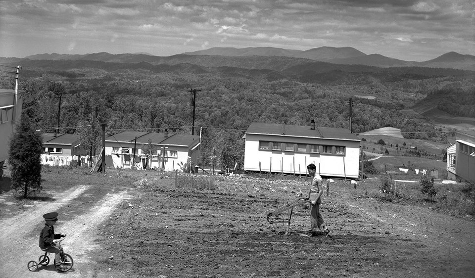 Oak Ridge resident diligently tending to his garden, while a spectator looks on in the 1940s a man uses a hand tool to plow home garden on hillside