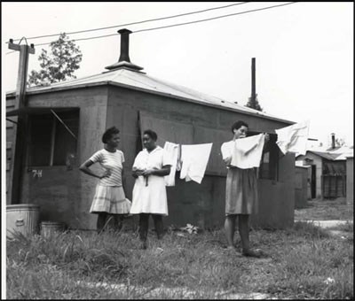 3 African American women stand outside of housing in Oak Ridge. 3 women stand next to a clothes line