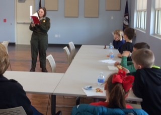 A ranger reading a book, students sitting at tables.