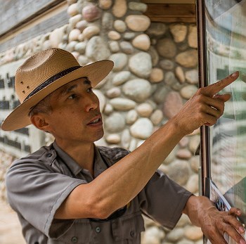 Ranger providing trailhead orientation Male park ranger pointing at map in bulletin board case