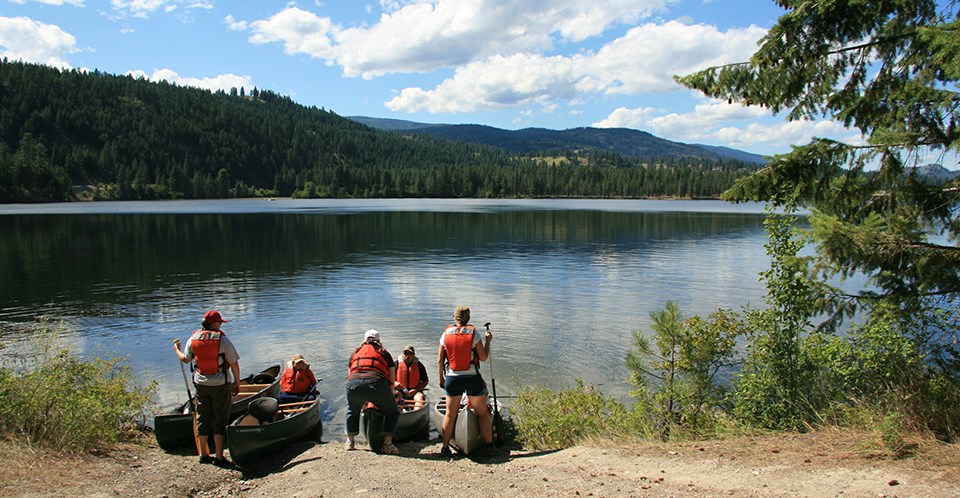 Canoeing at Lake Roosevelt a group of prepares to launch canoes into an evergreen-lined lake