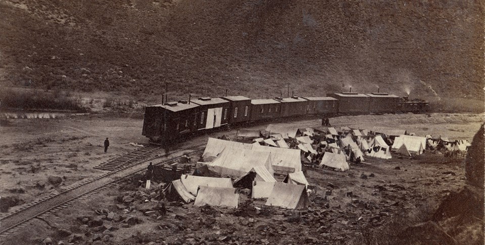 Chinese worker camp next to the Transcontinental Railroad historic photo of a group of white tents along the side of a railroad line