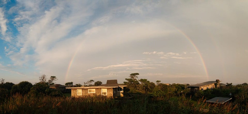 A rainbow is visible across a partially hazy and partially clear sky above houses glistening in the morning sunlight