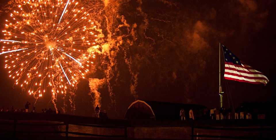 Fireworks at Fort McHenry National Monument & Historic Shrine fireworks in a night sky with observers watching below