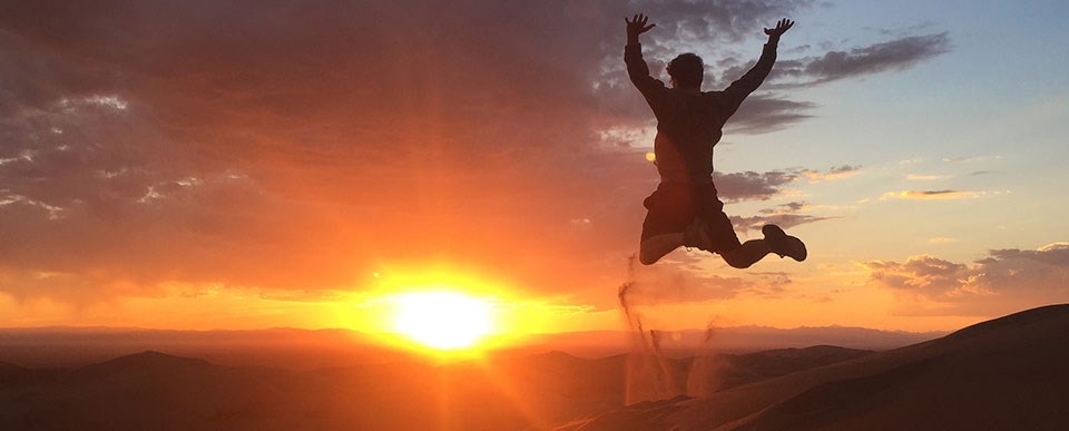 Man Jumping Off Star Dune at Sunset -- Great Sand Dunes NP&P man jumping off sand dune with sun setting in background