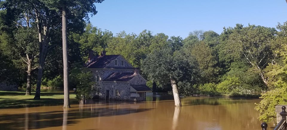 murky brown floodwaters cover the base of a historic two story stone and its nearby trees