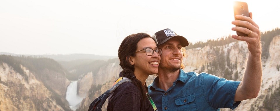 YELL Artist Point Selfie (NPS Jacob Frank) Two people taking a selfie overlooking a canyon and river