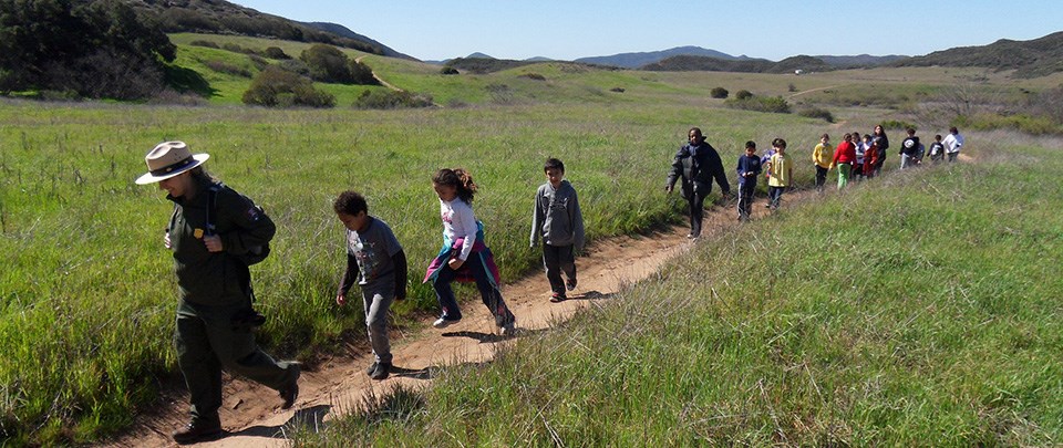 Ranger-led hike at Santa Monica Mountains Recreation Area a ranger leads school-age children along a dirt trail with rolling green hills in the background