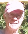 An elderly man, wearing a salmon colored hat faces the camera. He is wearing glasses and has white hair.
