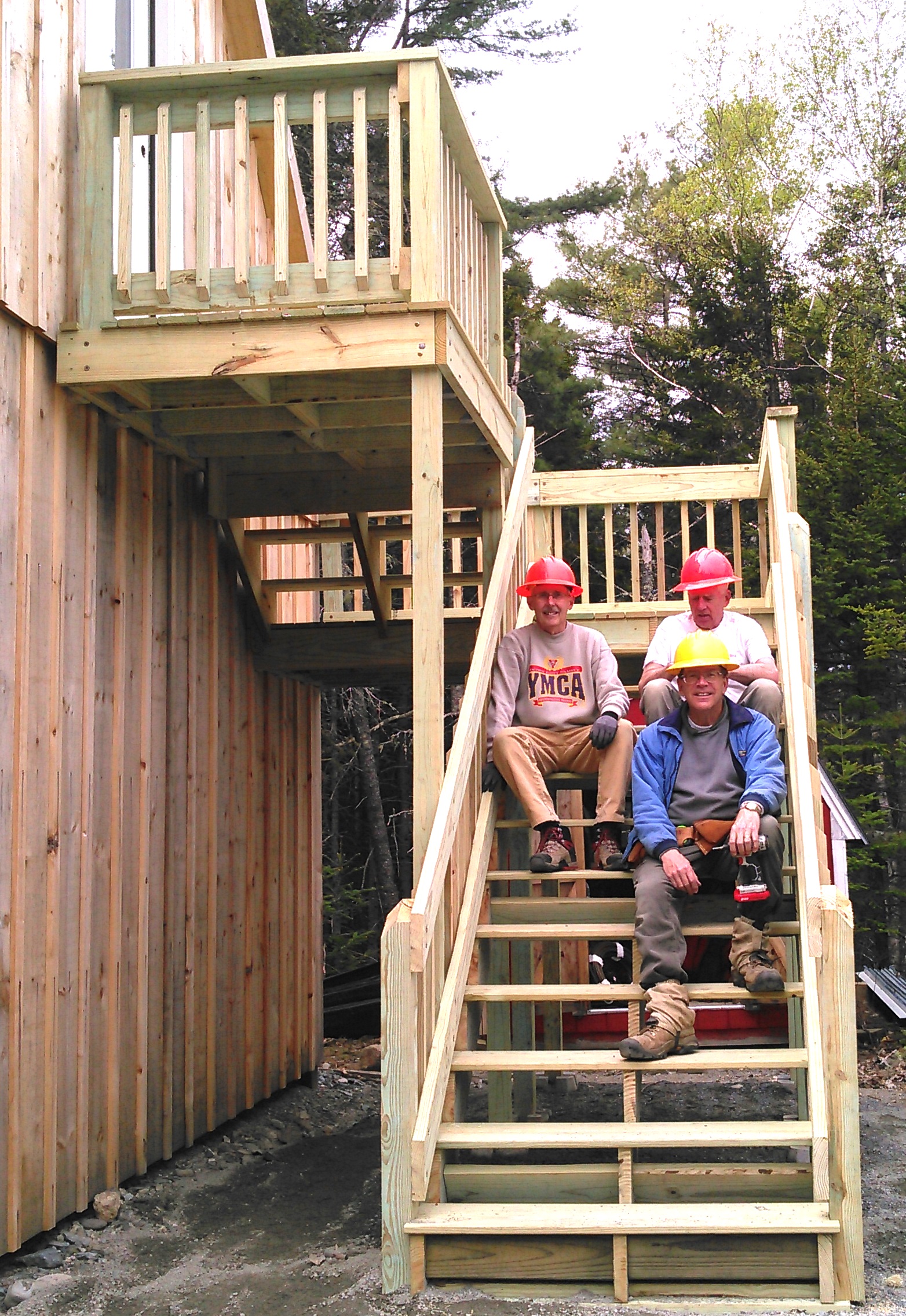 Stairs Built by Volunteers Three middle age men set facing the camera on bright wooden steps.