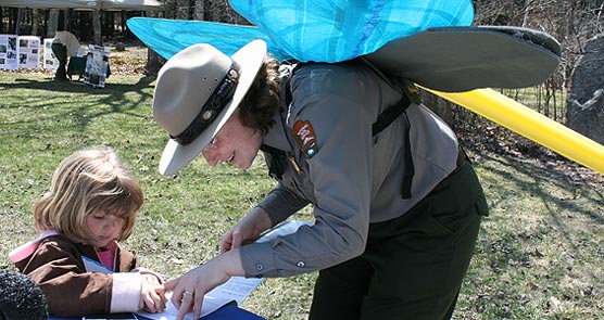 Park rangers wearing model dragonfly wings stamps child's book