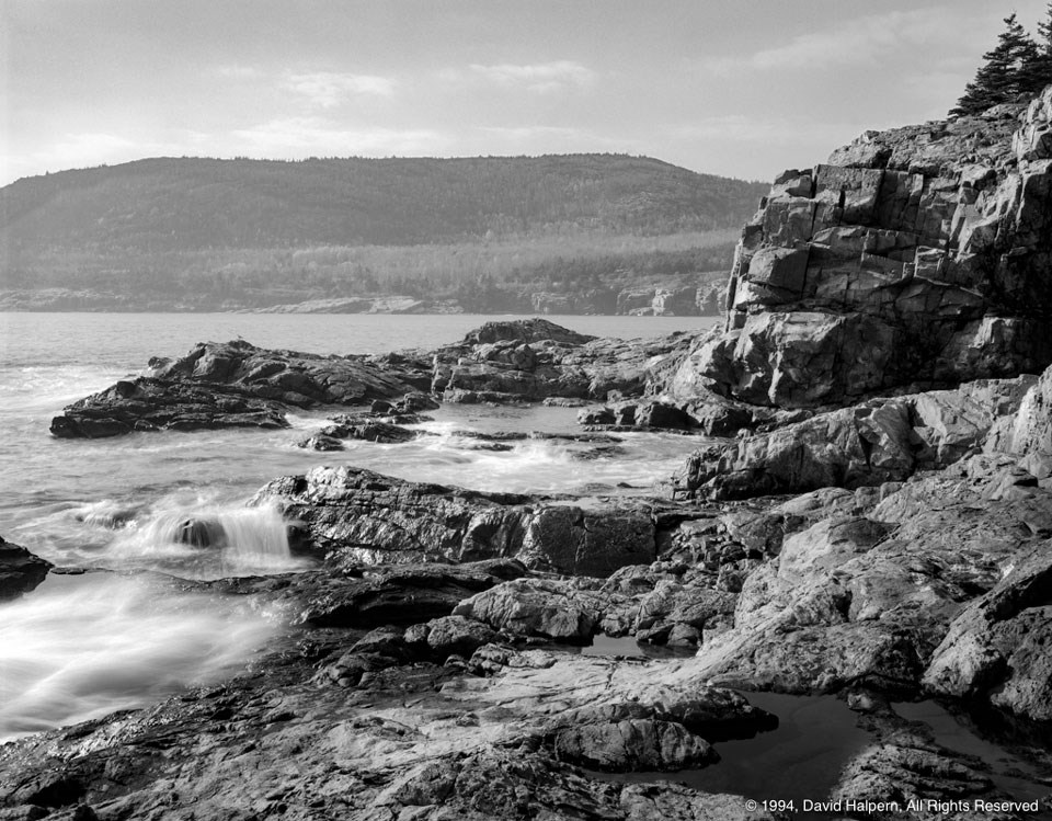 Rocky coastline with wooded mountain across water in distance