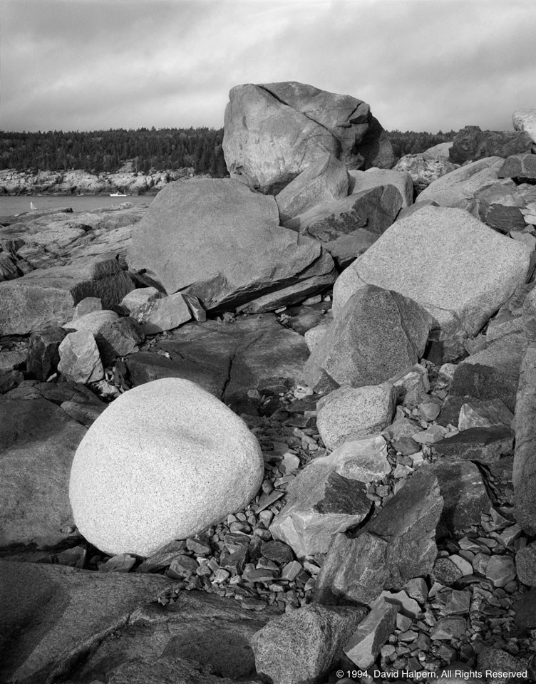 Jagged dark ocks along coastline with one smooth white boulder