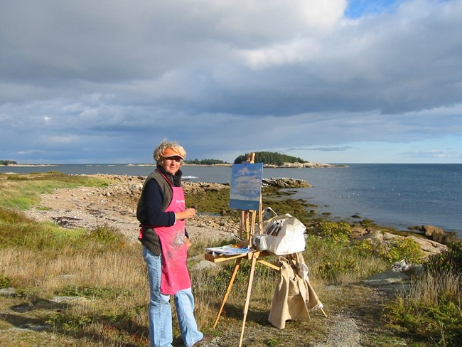 Whitlock Photograph of artist Priscilla Whitlock on the coastline with her easel