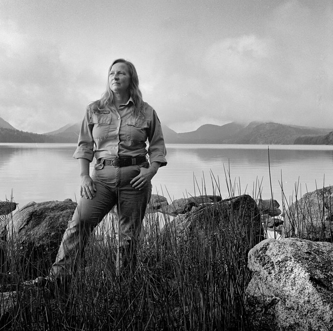 Female trail crew worker standing in front of Eagle Lake. She is looking off to her right and has a thumb in one pocket.