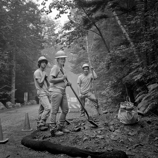 Black and white photograph of three trail crew workers on the side of a carriage road with shovels in their hands.