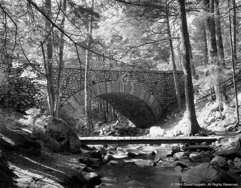 A narrow wood footbridge in foreground with an elegant stone bridge filling frame behind