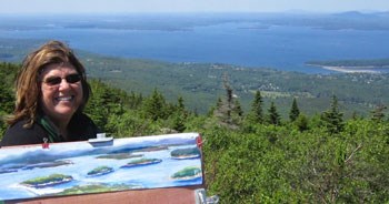 Woman holds painting of location depicted in image