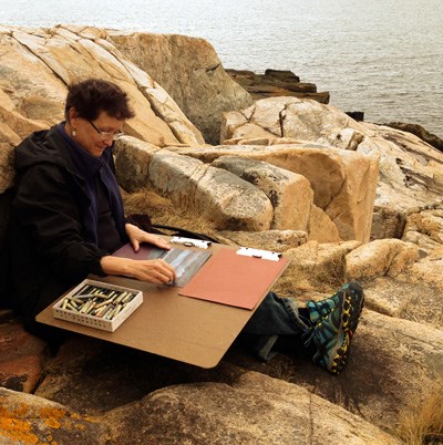 Woman with art board and materials prepares to work sitting on rocks along Atlantic coast