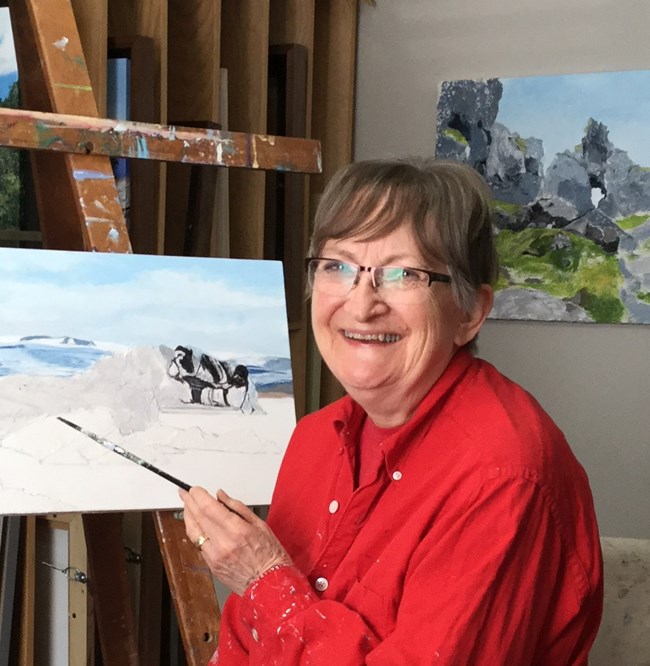 Picture of artist Joan Meade sitting down with a red shirt on