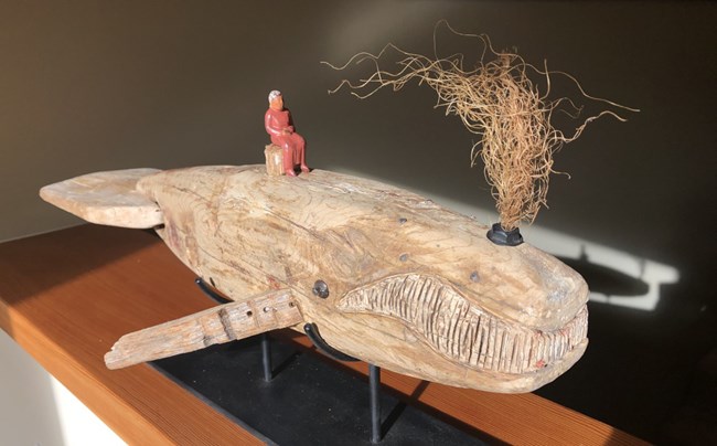 Artwork of a wooden whale spouting fiber from blow hole with a carved person on its back