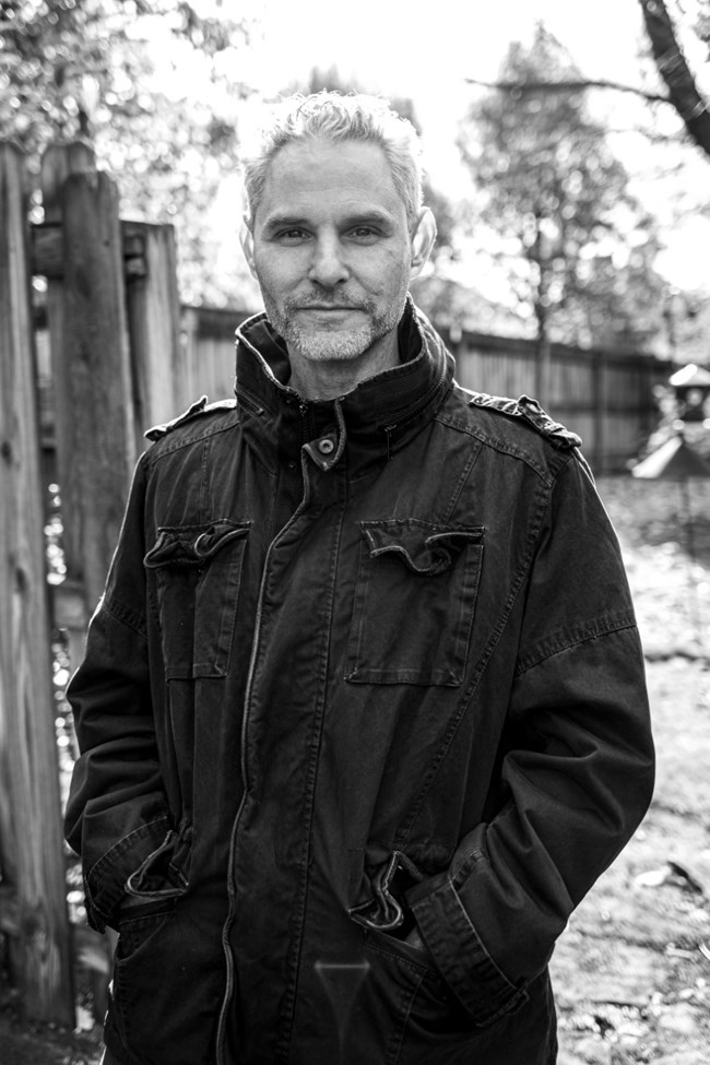Portrait of man in dark winter jacket standing outside by a fence