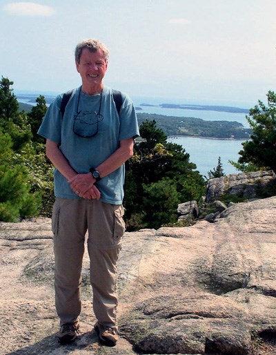 Man in T-shirt and cargo hiking pants poses with a backdrop of distant islands