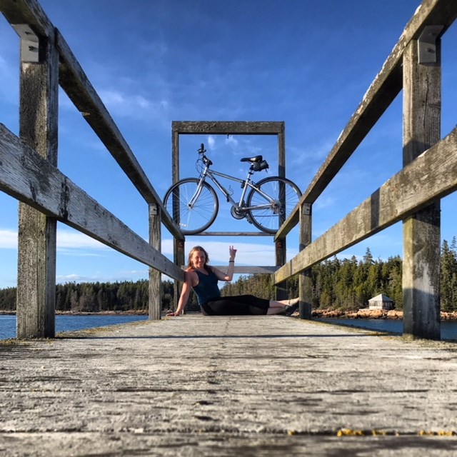 Woman sits under a bicycle perched between railings on a wooden pier