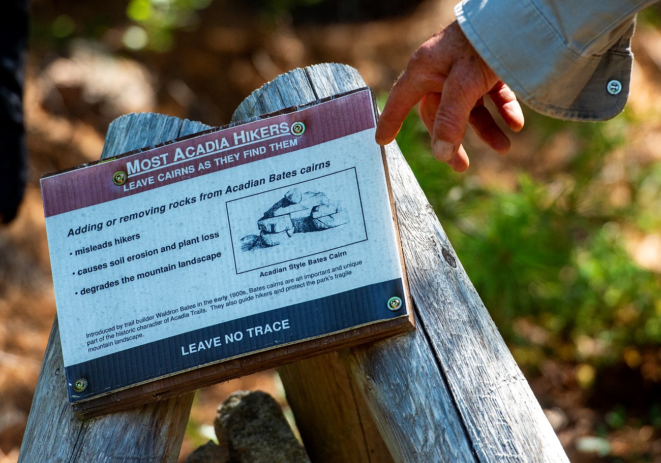 Person pointing to a wooden tripod with cairn information sign