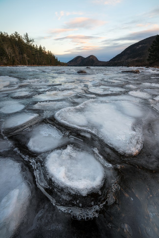 Winter landscape photo of frozen Jordan Pond with the Bubbles mountains in the distance