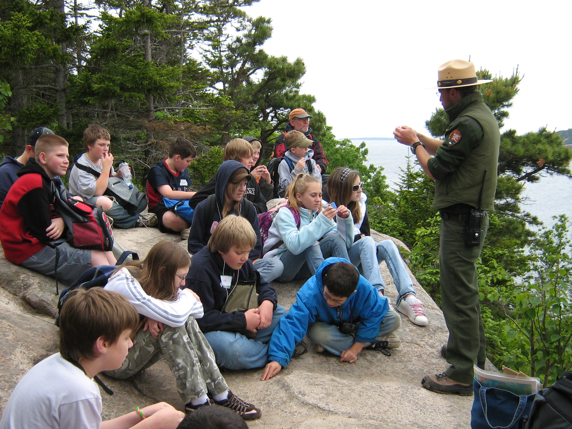 Ranger stands on rock ledge with students sitting nearby.
