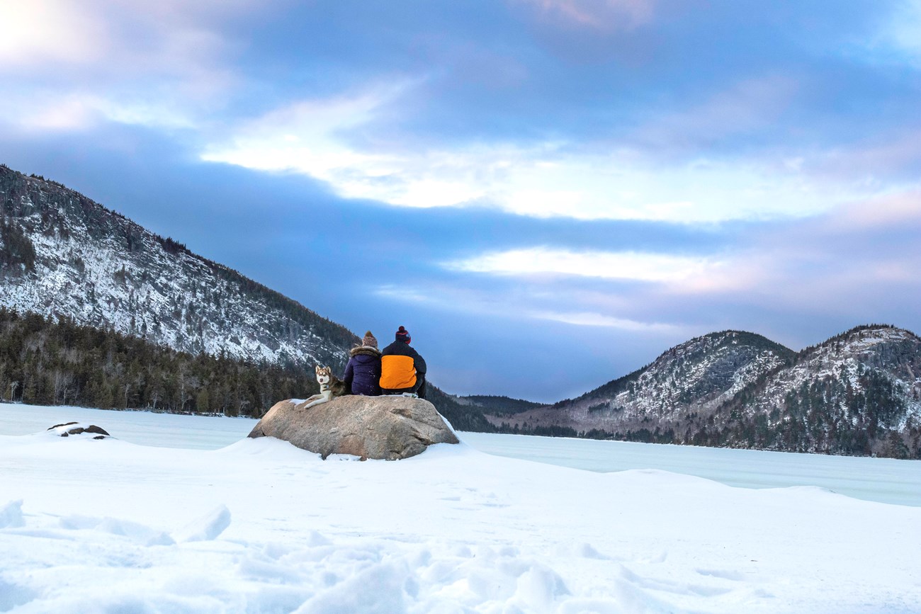 Winter hikers sit on rock in front of Jordan Pond.