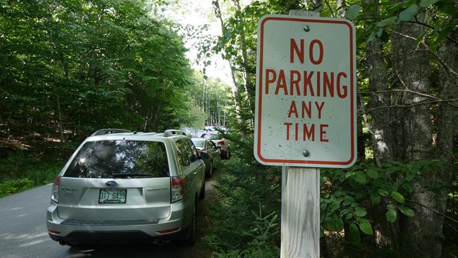Visitor vehicles defy a no parking sign on a narrow road