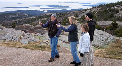 Four people stand on a trail on a mountain using a global positioning system unit. Four people stand on a trail on a mountain using a global positioning system unit.
