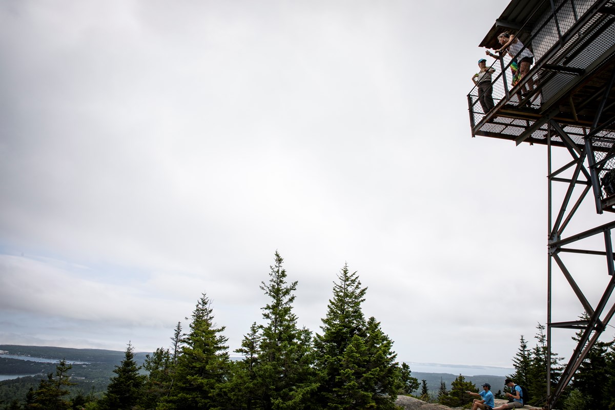 A fire lookout tower on a summit with people underneath and on a platform