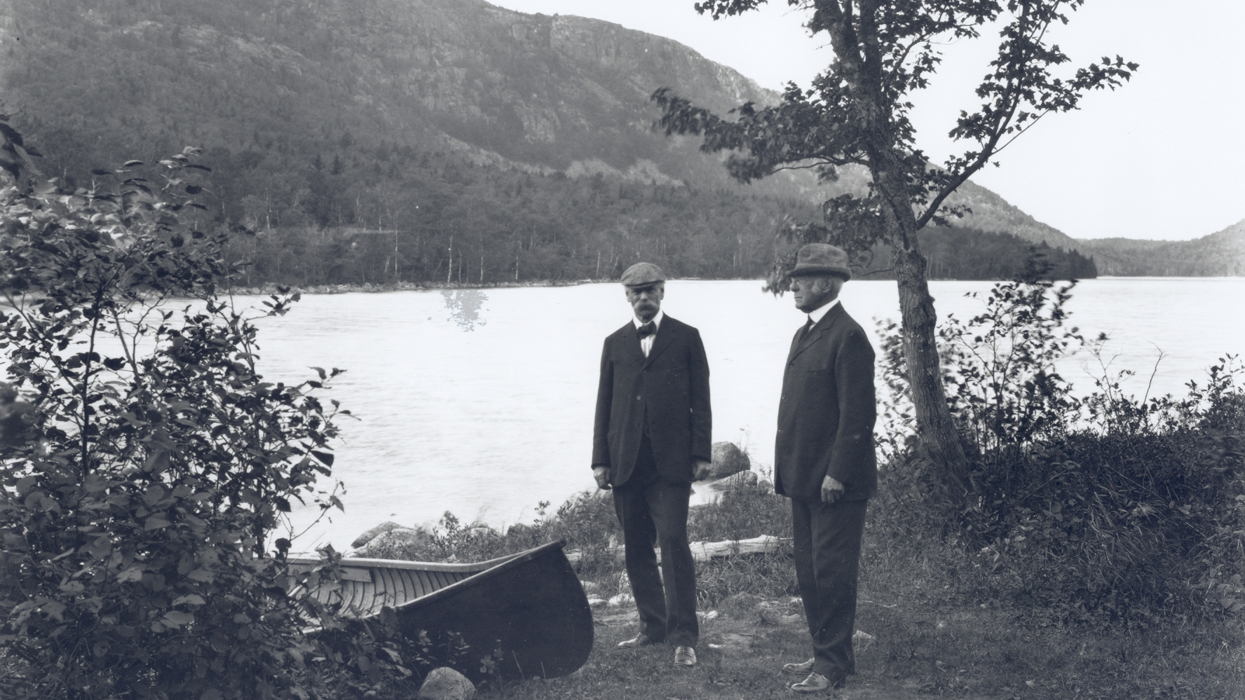 Two people standing in front of a boat near a lakeshore