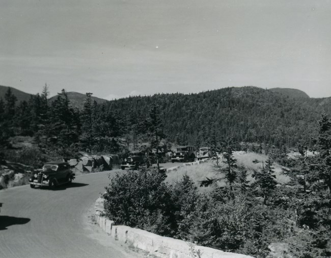 Historic photograph of motor road with cars lining edge