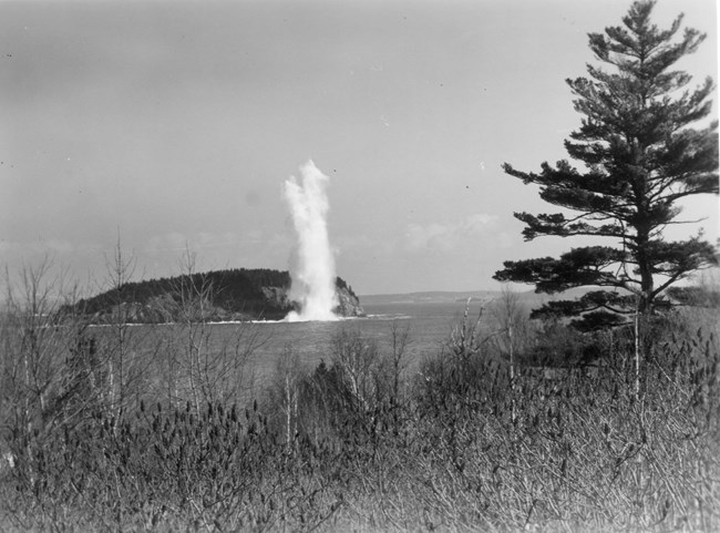 an explosion of water in front of an island in a black and white photo