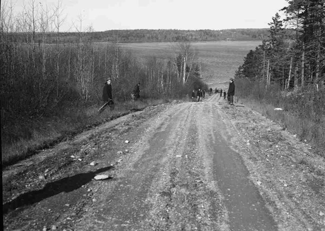 Construction workers stand along the edge of a unpaved road