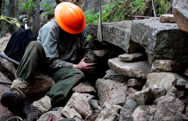 Trail crew member fits smaller rocks to repair a trail