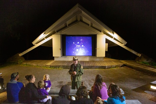 a ranger talks to a family in front of a screen at night