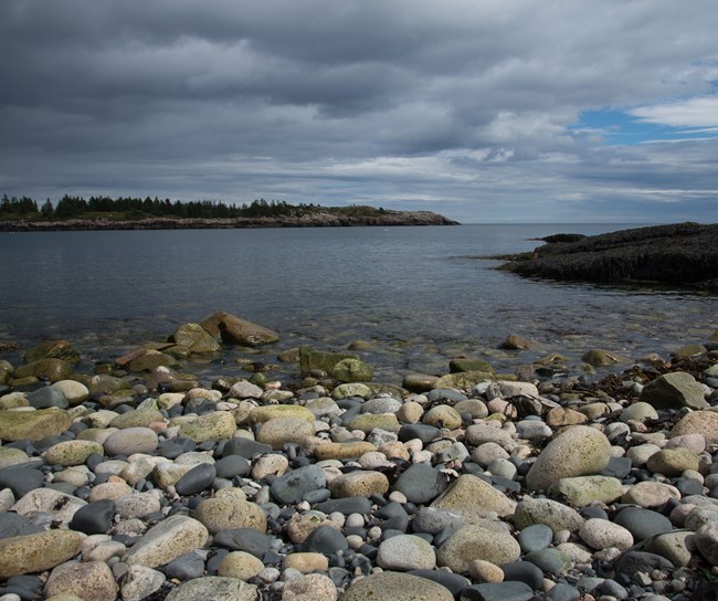 Cobblestones line an ocean shore on a cloudy day.