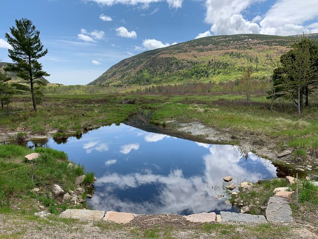 blue sky and clouds reflecting in water with mountain in the back