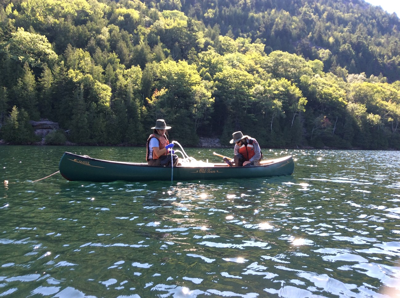 two rangers in a canoe on a lake placing a long hose into the water