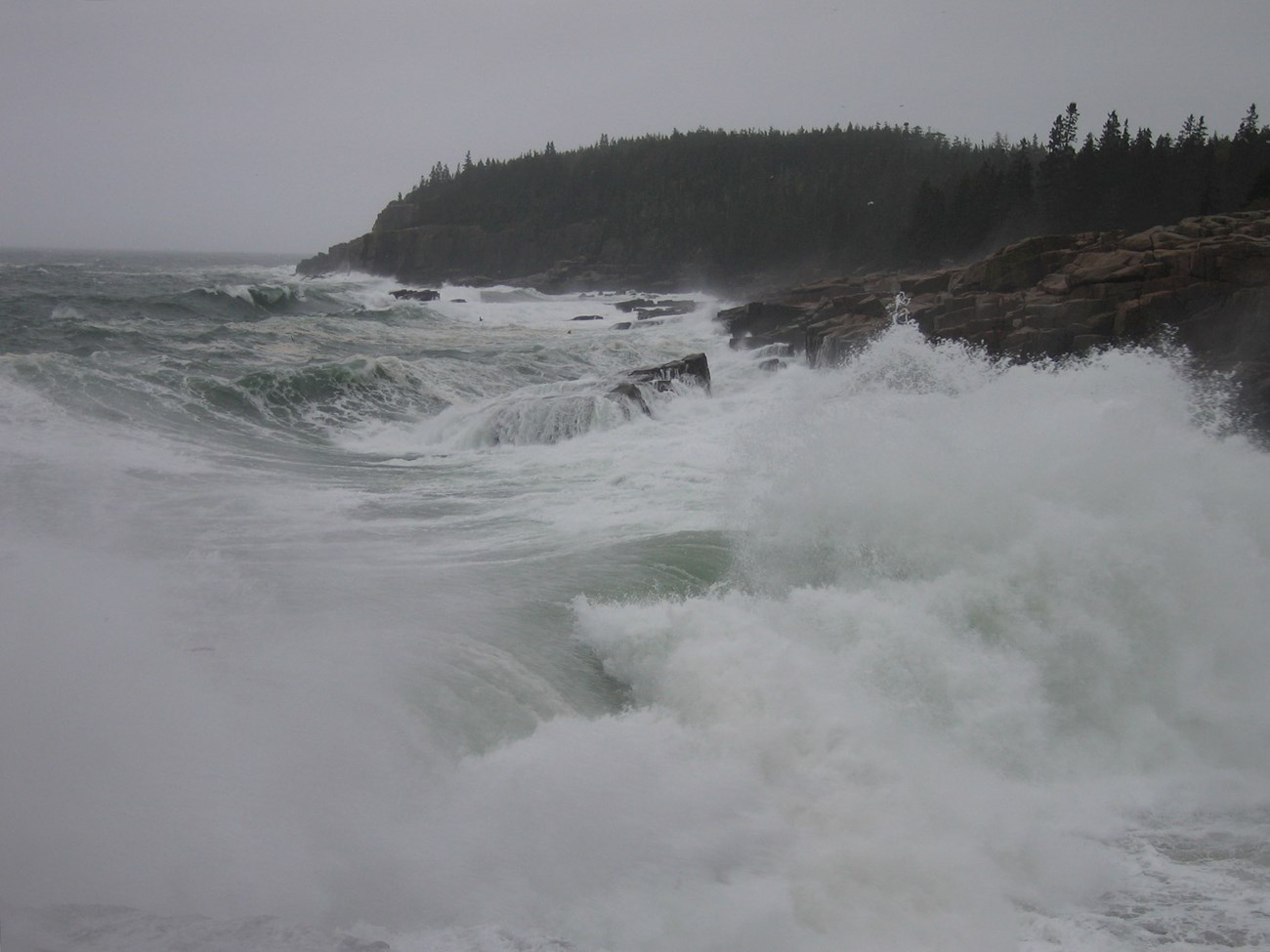 rough seas crash into dark cliffs in the rain