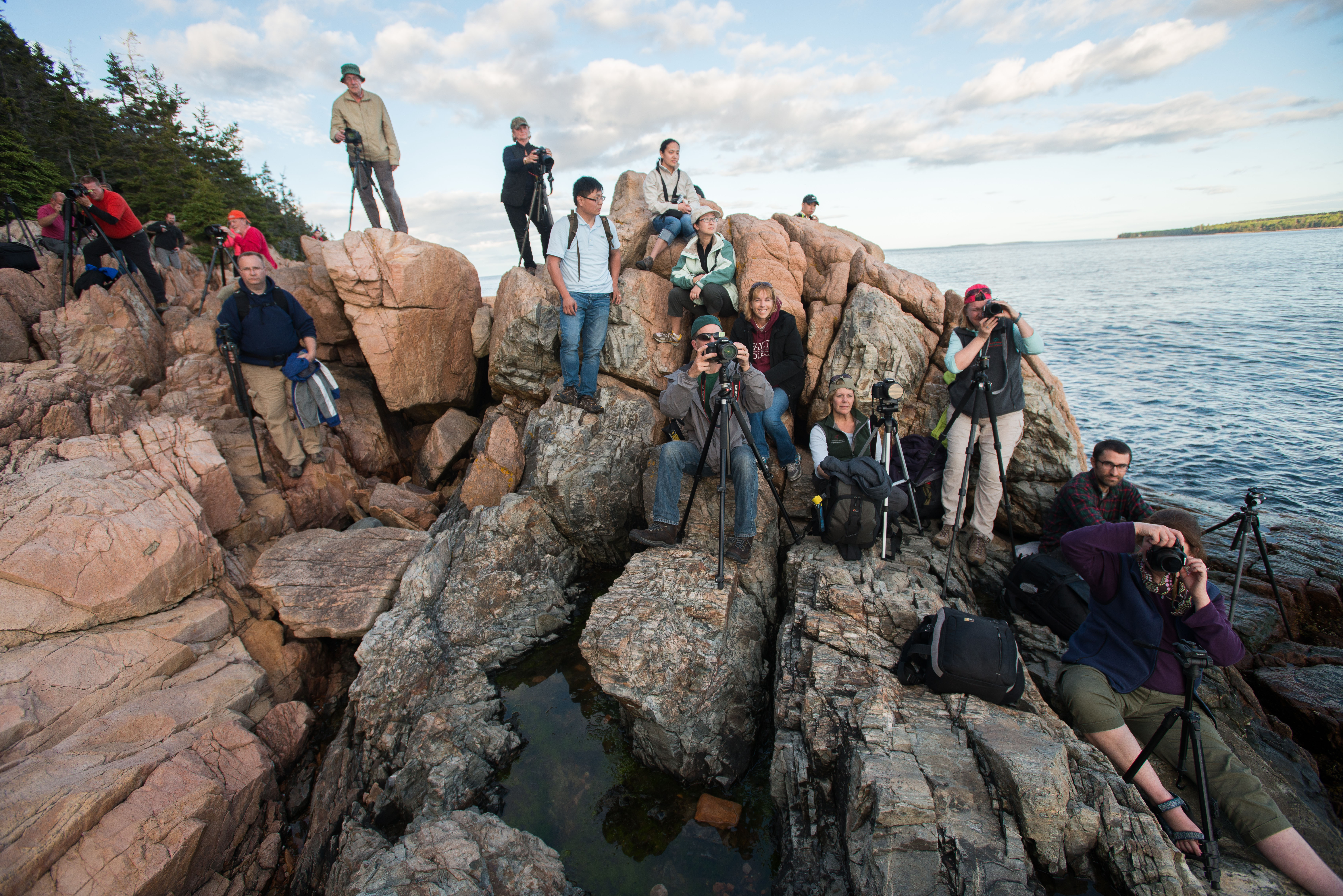 Dozens of photographers position themselves along a rocky shoreline