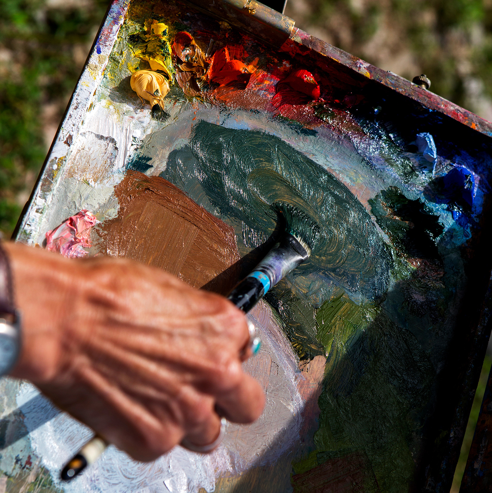 An artist hand and paint brush mixes colors on a palette