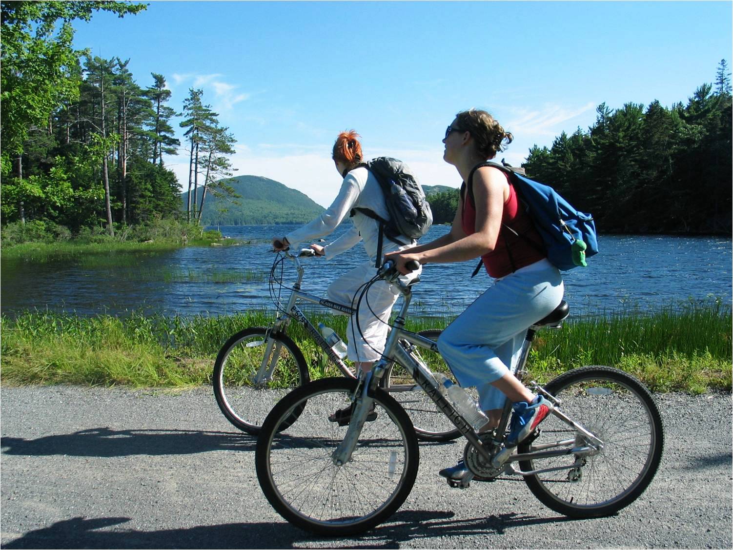 Two female presenting people ride their bikes in Acadia National Park.