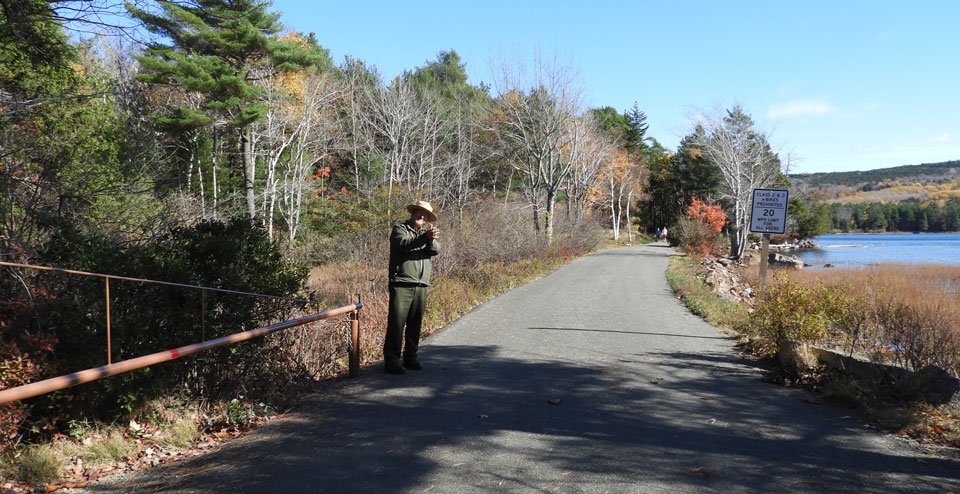 an employee in uniform stands with open arms in front of carriage road gate